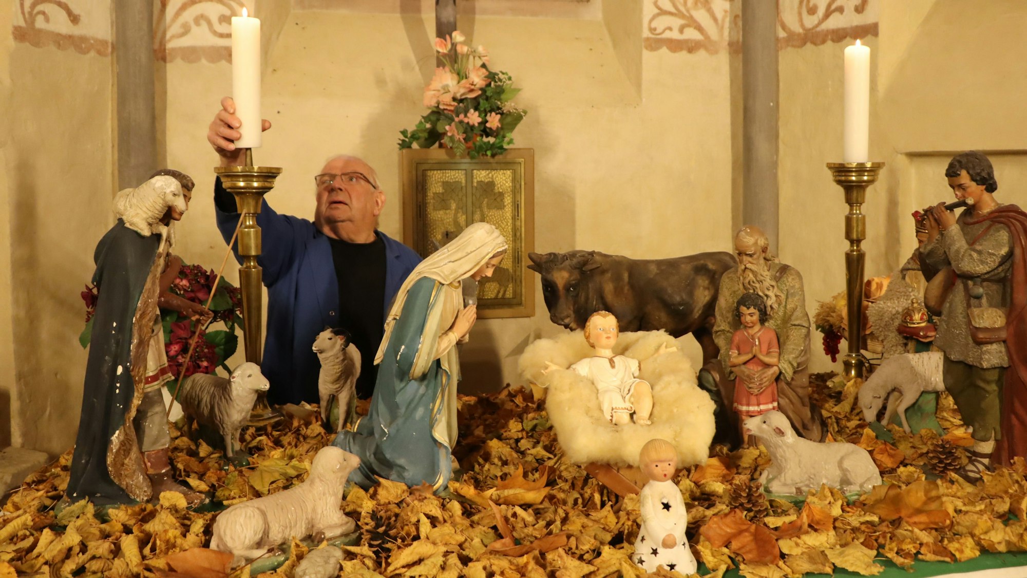 Ein Mann steht hinter einer Weihnachtskrippe und entzündet eine große Kerze.