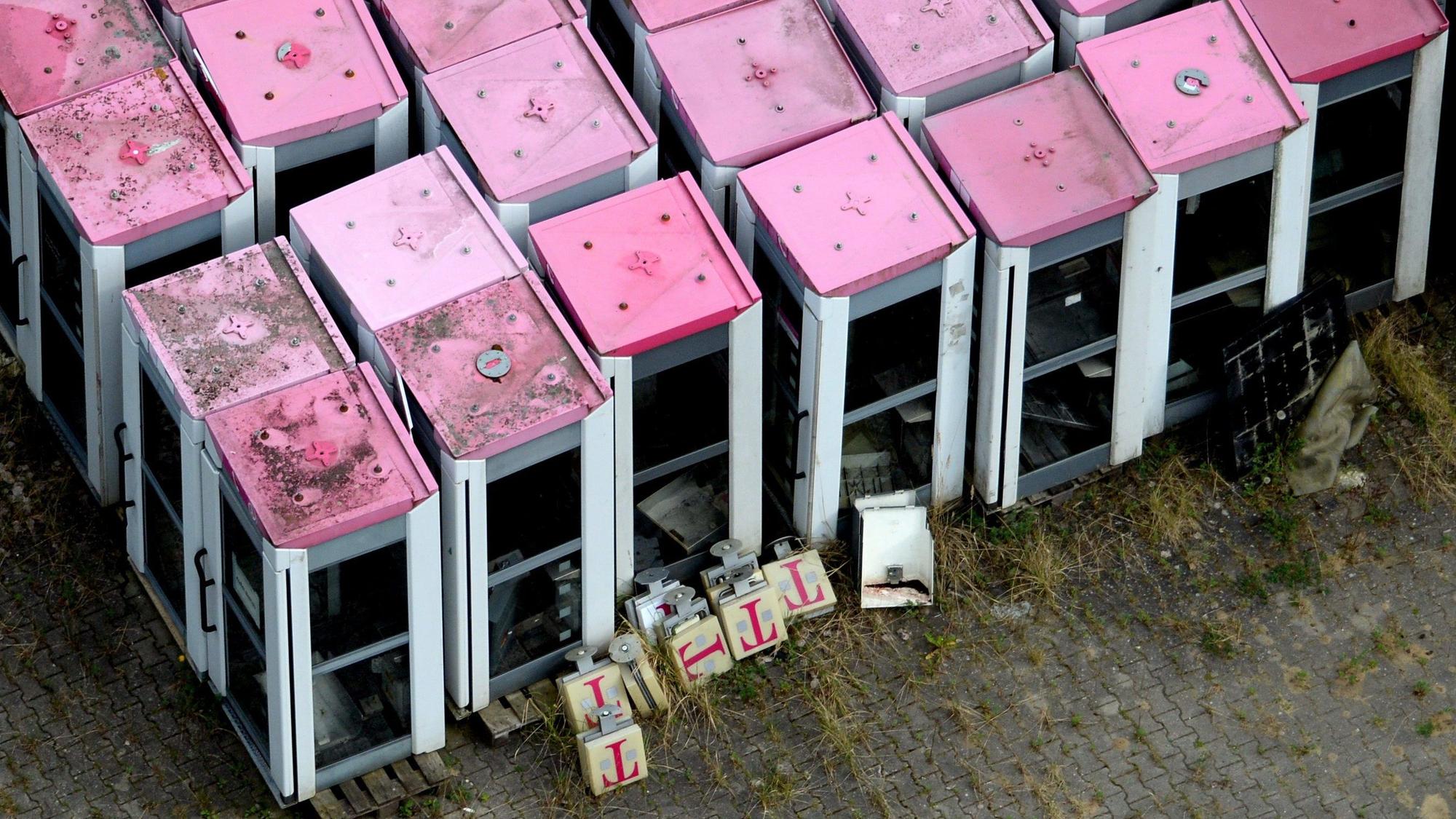 Die Luftbildaufnahme zeigt ausrangierte Telefonzellen der Telekom mit magenatfarbenen Dächern.