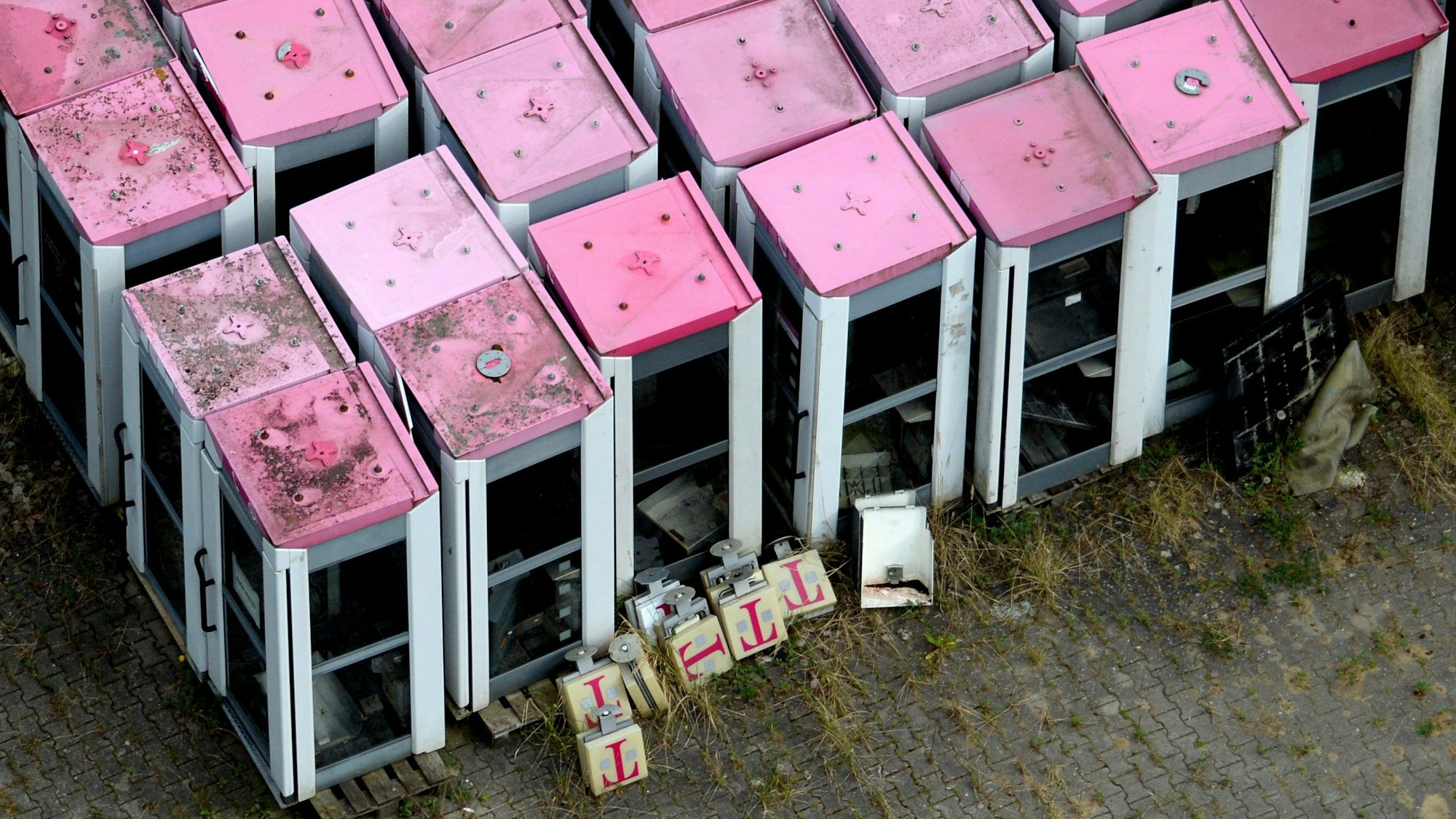 Die Luftbildaufnahme zeigt ausrangierte Telefonzellen der Telekom mit magenatfarbenen Dächern.