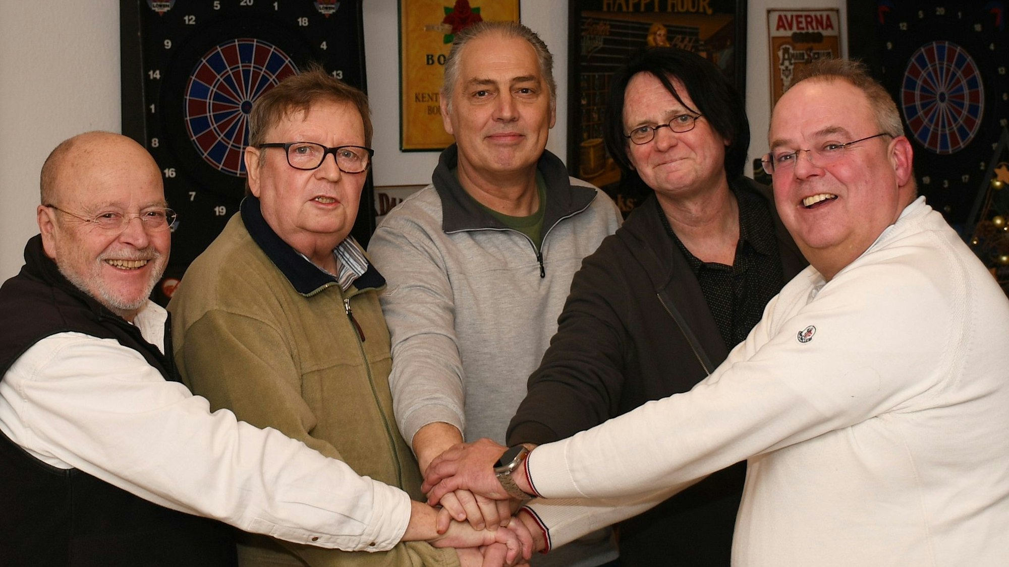 Die fünf Männern stehen nebeneinander und haben die Hände als Zeichen des Zusammenhalts in der Mitte zusammengelegt.