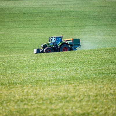 Ein Traktor mit einem Streuaufsatz verteilt Dünger auf einem Feld.