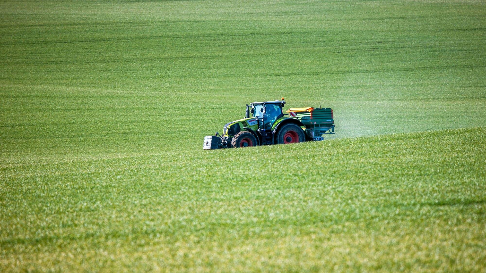 Ein Traktor mit einem Streuaufsatz verteilt Dünger auf einem Feld.
