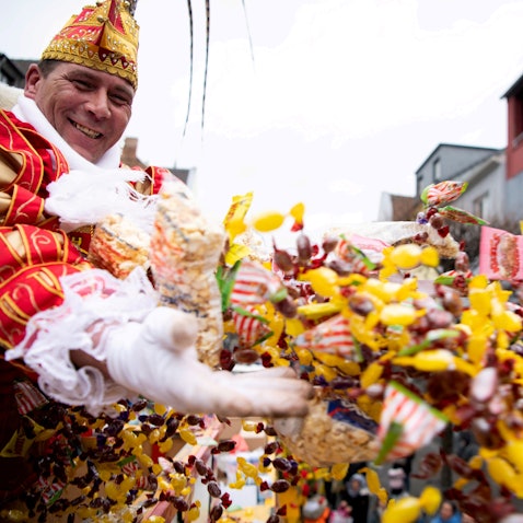 Das Bild zeigt eine Tollität, wie sie mit beiden Händen eine große Anzahl an Kamelle wirft.