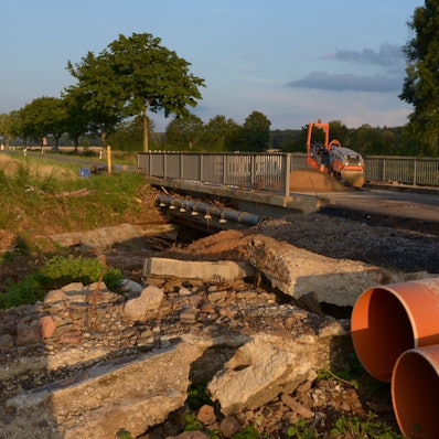 Neben der Orbachbrücke bei Palmersheim, die durch das Hochwasser schwer beschädigt wurde, liegen Betontrümmer. Auf der Fahrbahn stehen zwei Bagger für Reparaturarbeiten.