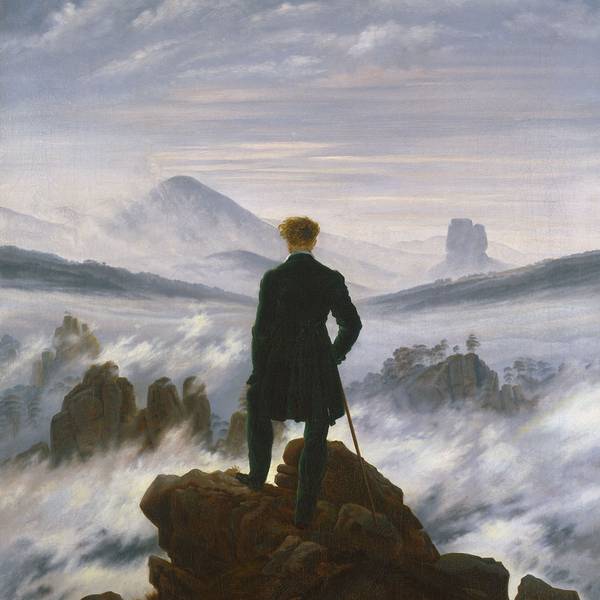 Ein Mann steht auf einem Gipfel und schaut auf eine neblige Landschaft.