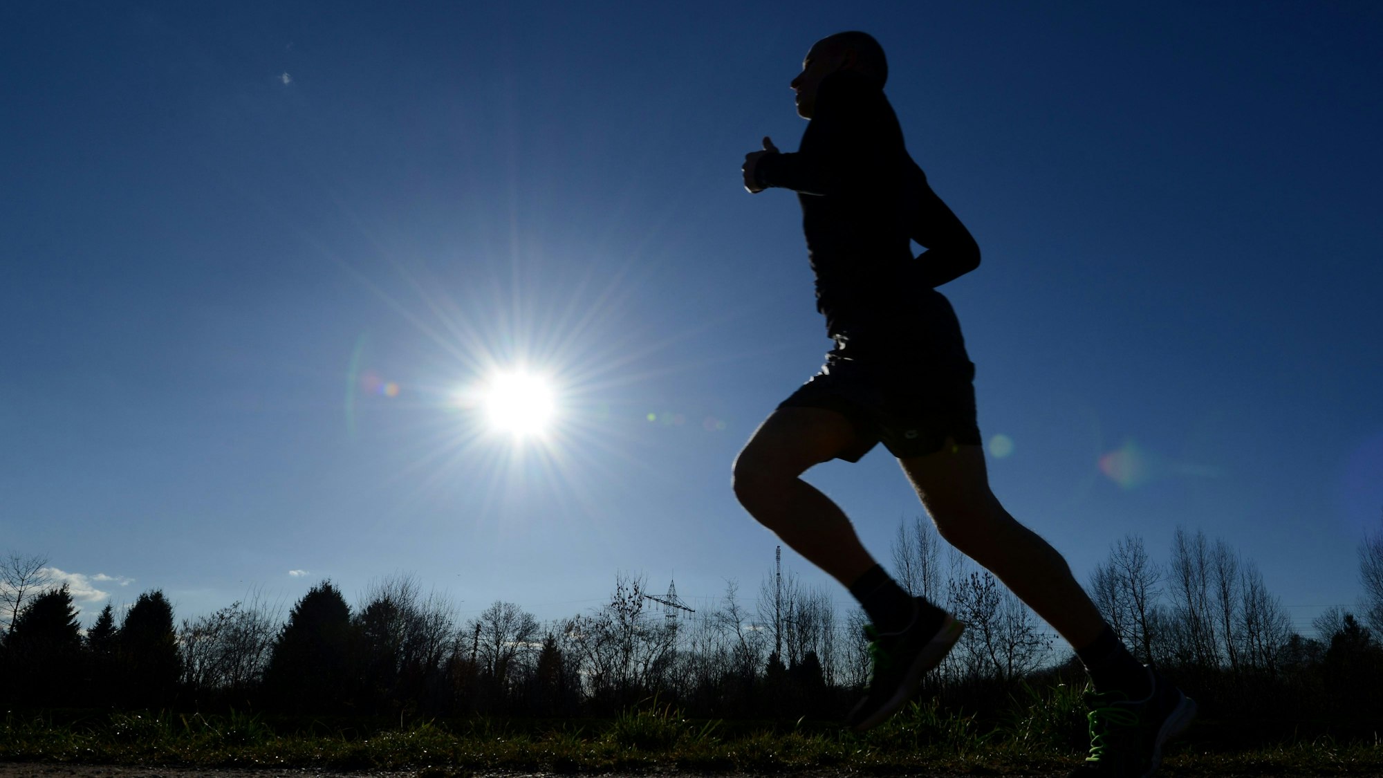 Ein Jogger läuft bei blauem Himmel und strahlendem Sonnenschein an der Dreisam in Freiburg (Baden-Württemberg).