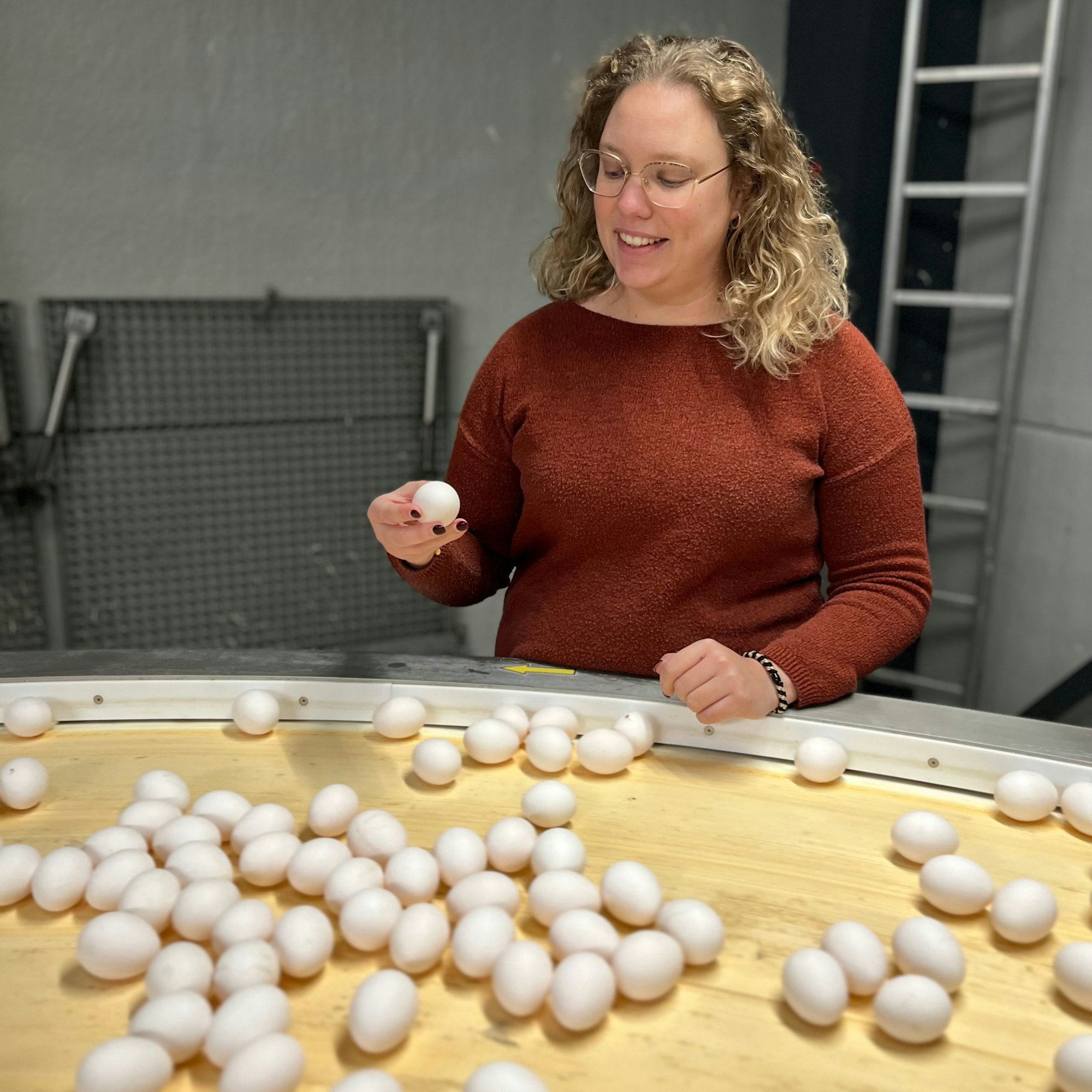 Jasmin Schleder bei der Kontrolle von Hühnereiern, die vor ihr liegen. Ein Ei hat sie in der rechten Hand.