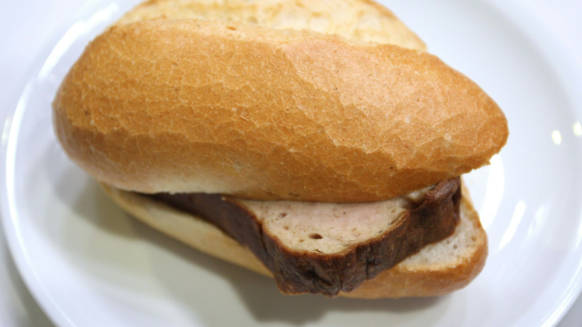 Ein Leberkäs-Brötchen auf einem weißen Teller.