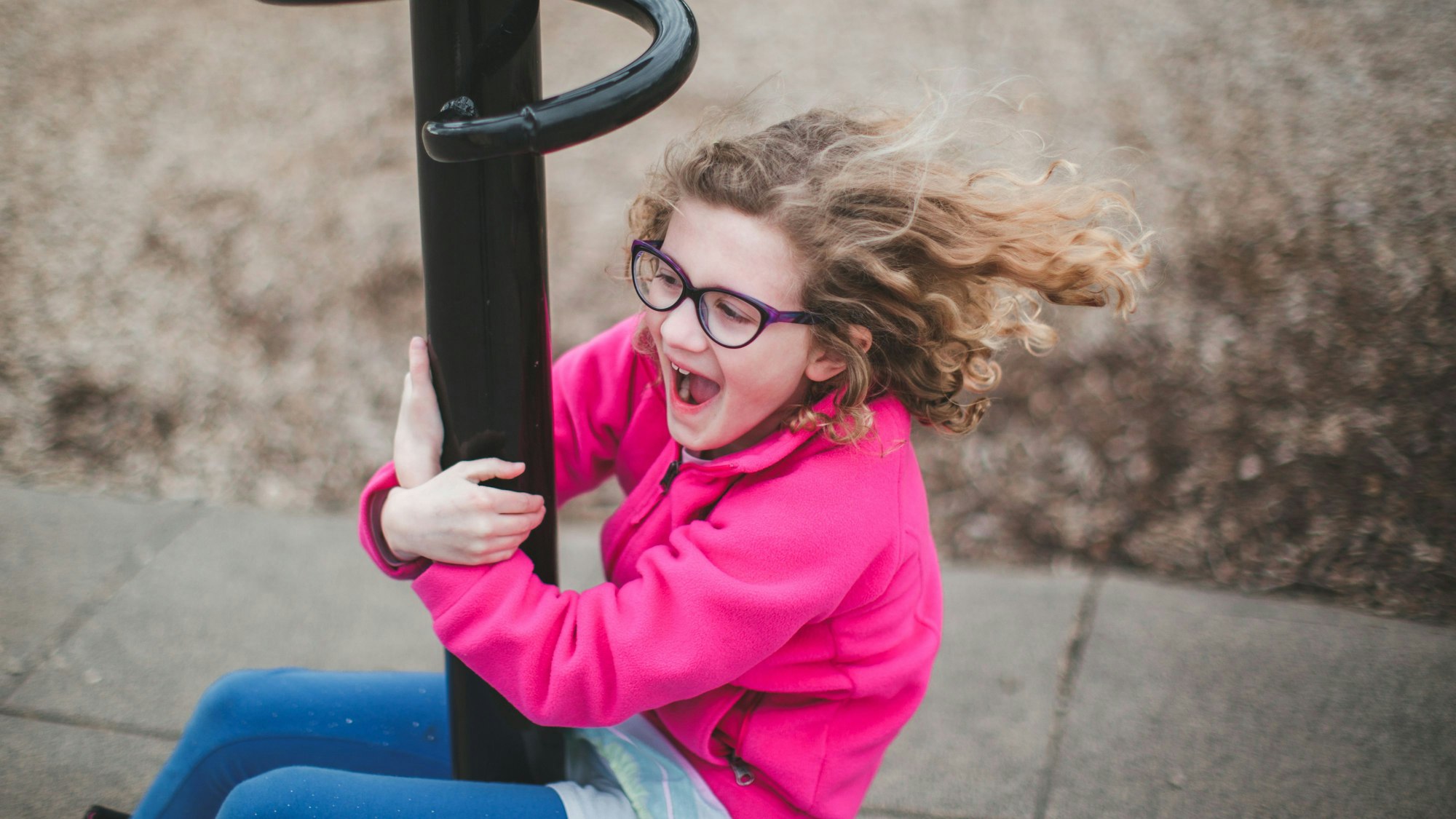 Ein knapp sechs- bis siebenjähriges Kind, das eine Brille trägt, spielt auf einem Spielplatz