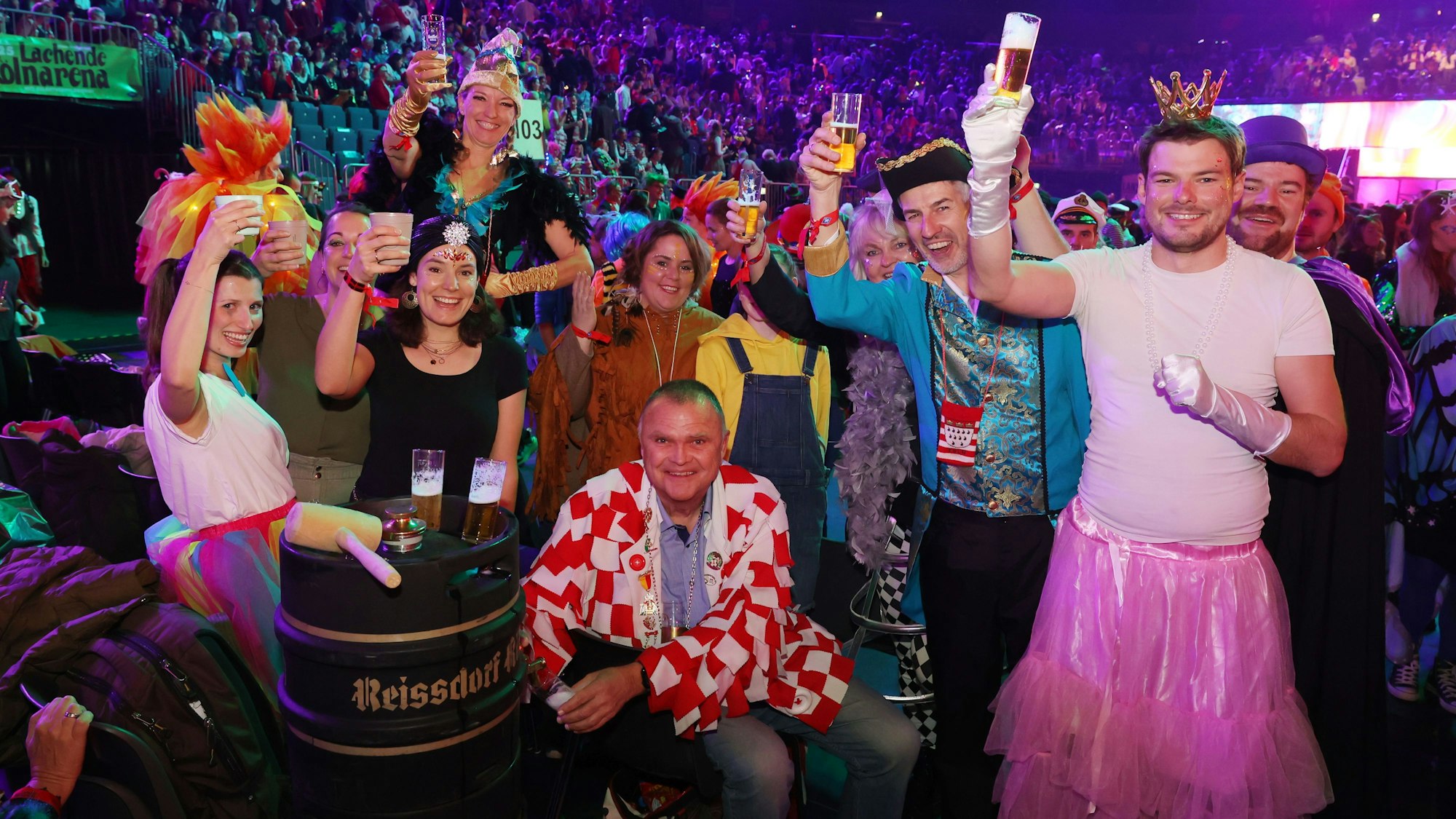 Verkleidete Menschen in der Lanxess-Arena prosten der Kamera mit Kölsch zu.