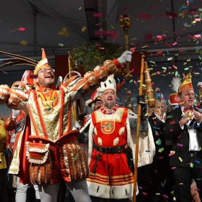 Das Dreigestirn hebt begeistert die Arme, singt und lacht. Auf die Bühne fällt ein Konfettiregen nieder.