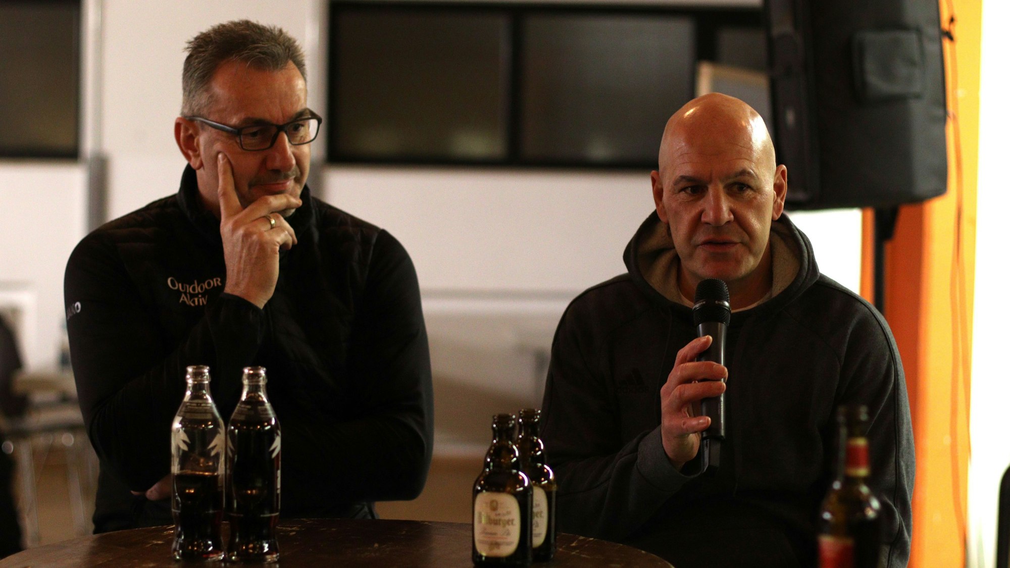 Jörg Piana spricht ins Mikrofon, Dieter Pütz legt den Finger ans Gesicht.