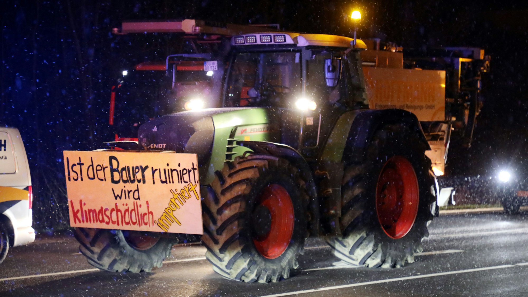 Ein Traktor mit einem Schild steht auf einer Straße im Schneetreiben.