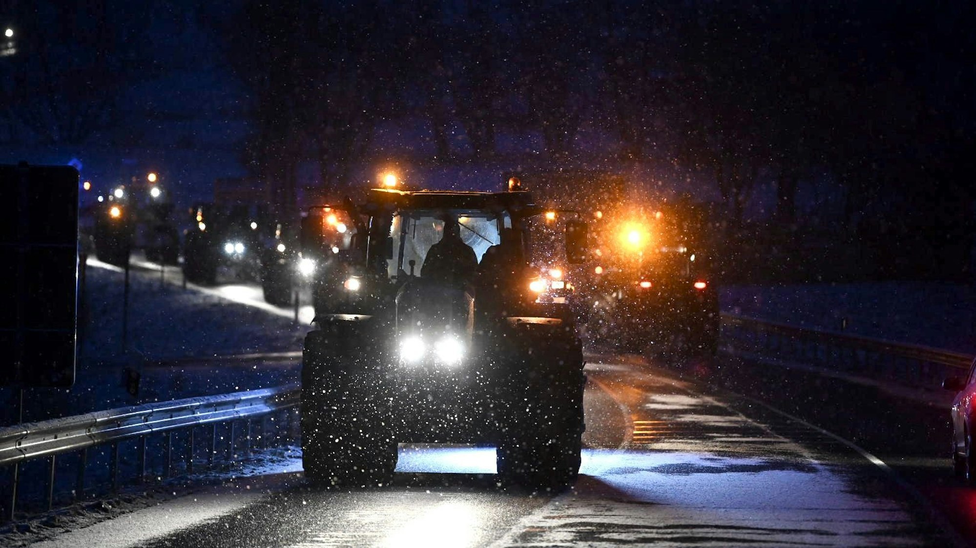 In der Dunkelheit und im Schneegestöber fährt eine Traktorkolonne.
