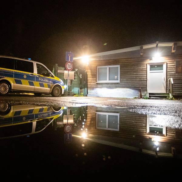 Die Polizei steht in der Dunkelheit vor einer beleuchteten Flüchtlingsunterkunft.
