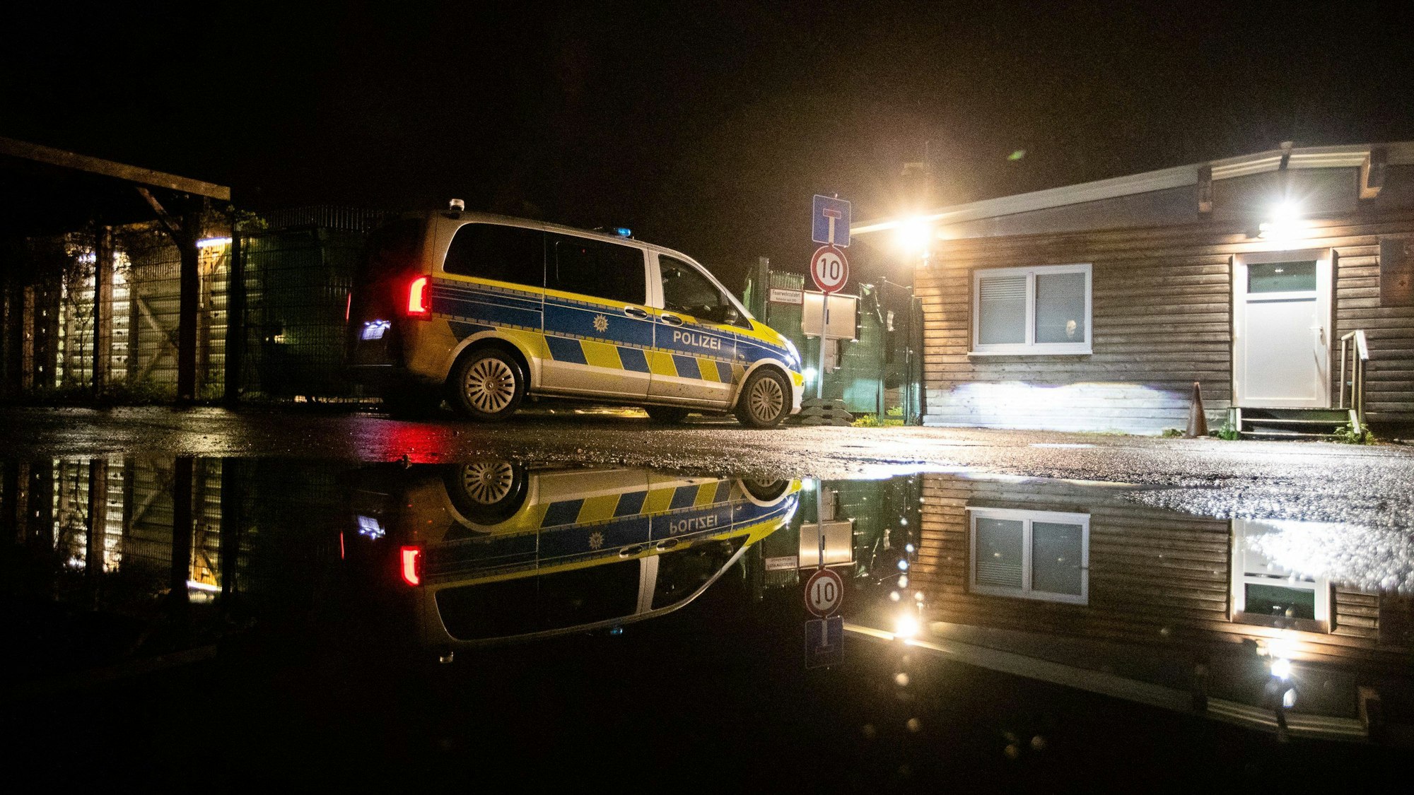 Die Polizei steht in der Dunkelheit vor einer beleuchteten Flüchtlingsunterkunft.