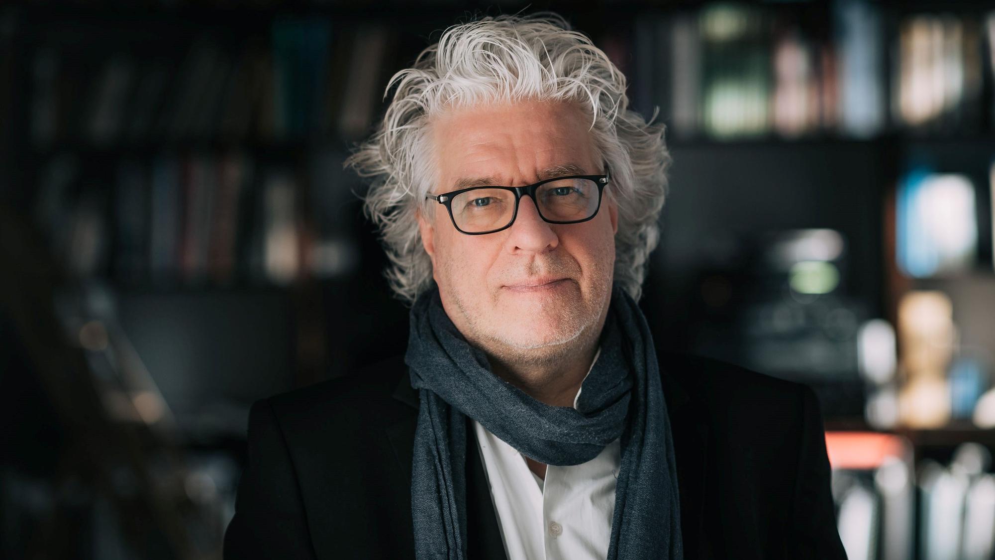 Christoph Spering steht vor einer Bücherwand.