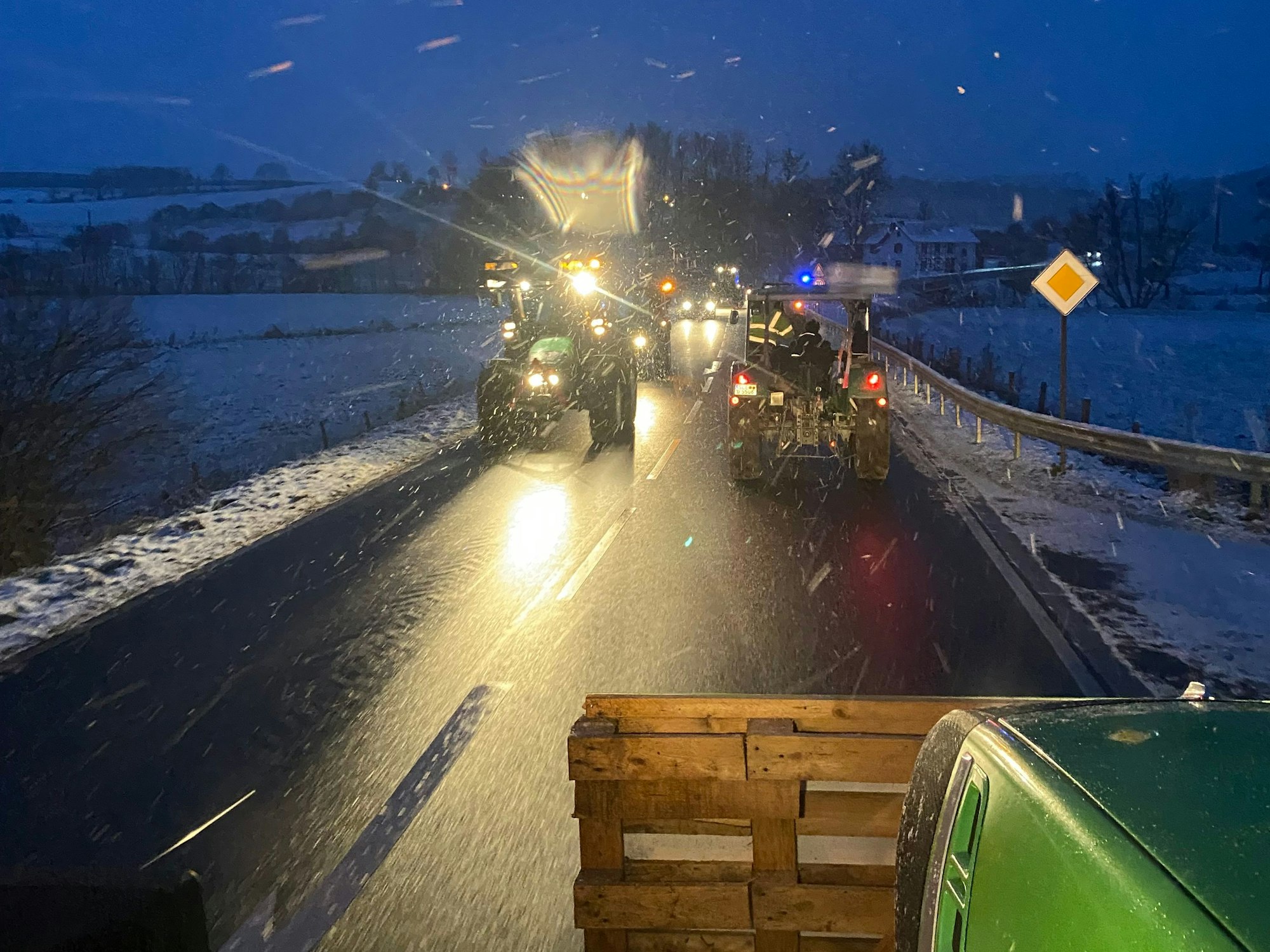 Im Schnee fahren viele Traktoren über die Landstraße.