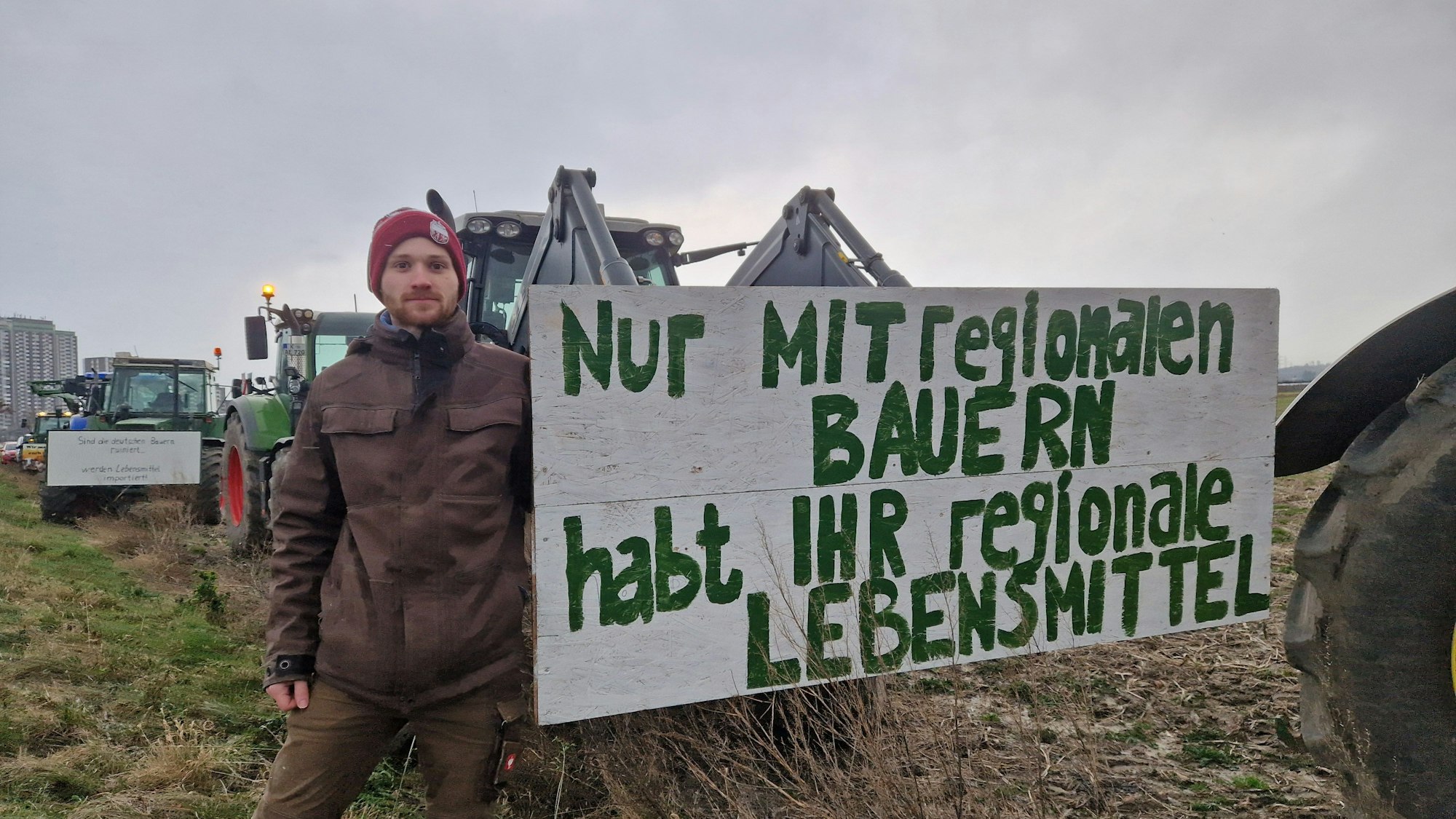 Der Landwirt Severin Nesseler steht neben seinem Traktor. Davor steht ein Transparent mit der Aufschrift: "Nur mit regionalen Bauern habt ihr regionale Produkte."
