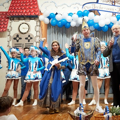 Das Prinzenpaar aus Scheven steht im Ornat auf der Bühne und lässt sich von Ortsvorsteher Hans Reiff feiern. Im Hintergrund steht eine Tanzgruppe, die Bühne ist mit blauen und weißen Luftballons geschmückt.