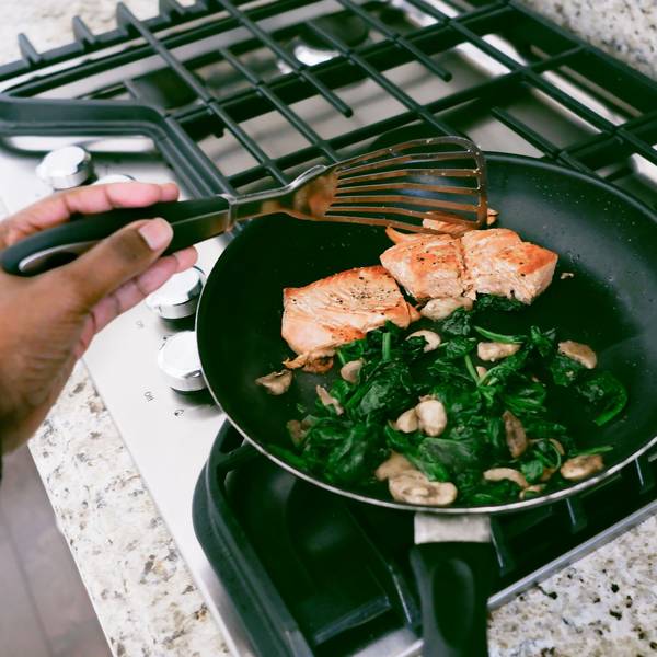 Eine Frau kocht Lachs mit Spinat in der Pfanne.