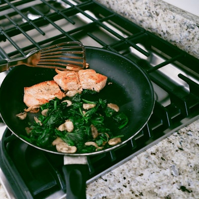 Eine Frau kocht Lachs mit Spinat in der Pfanne.