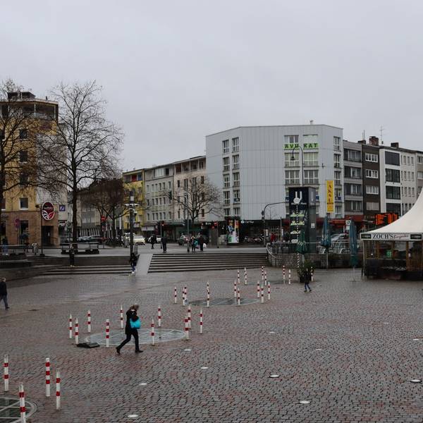 Wenige Fußgänger queren einen Platz mit einem zeltartigen Lokal.