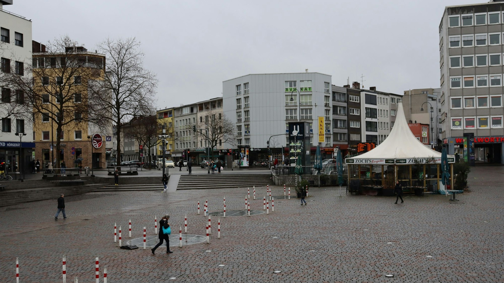 Wenige Fußgänger queren einen Platz mit einem zeltartigen Lokal.