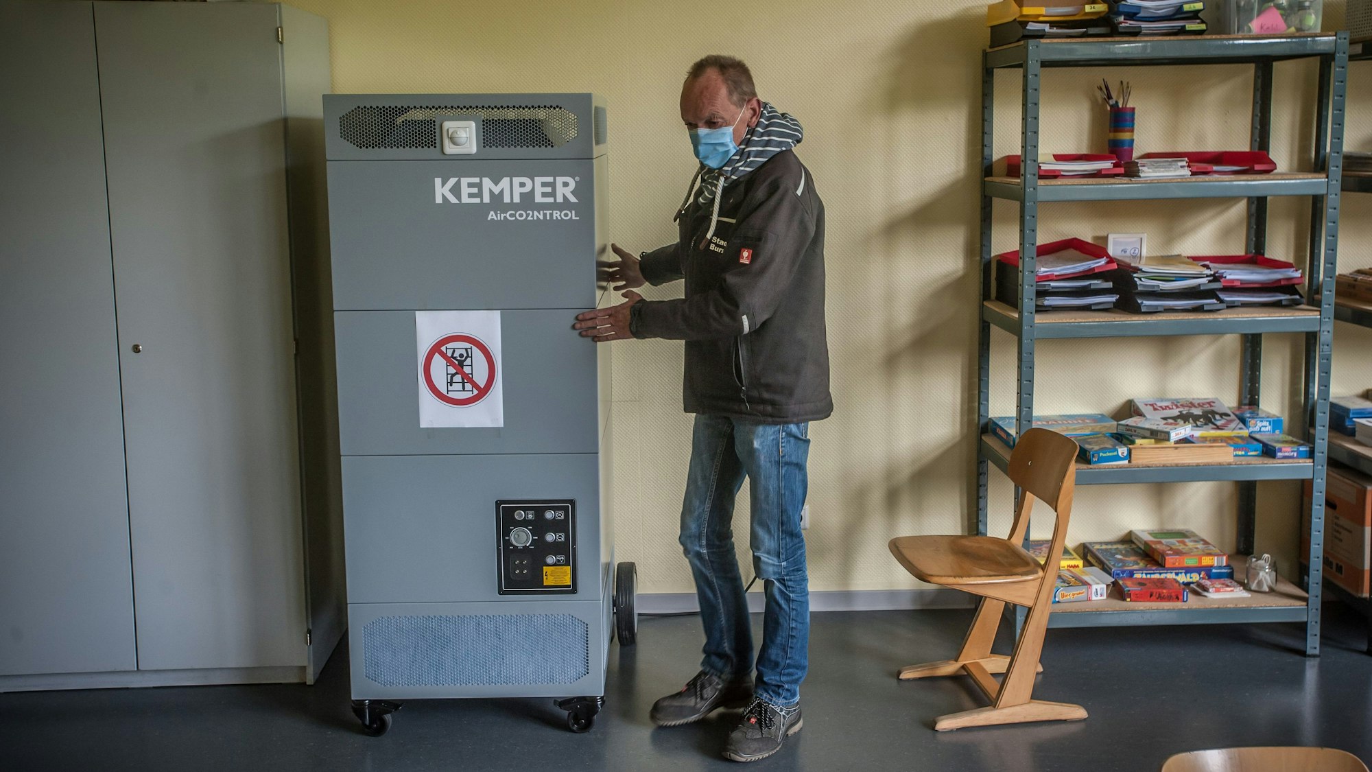 Ein Mann schiebt eine große Luftfilteranlage durch ein Klassenzimmer.