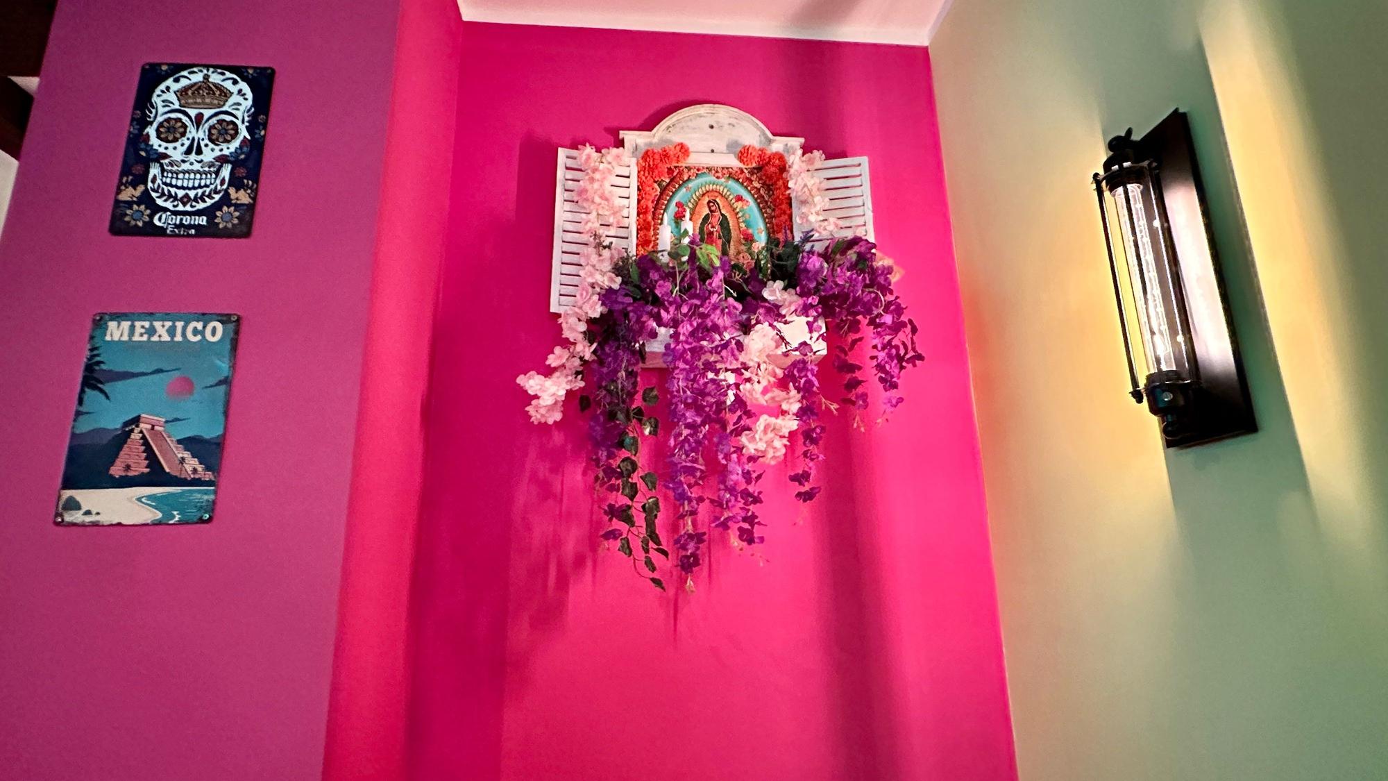 An einer pink gestrichenen Wand hängen Bilder und Wandschmuck aus Mexiko.