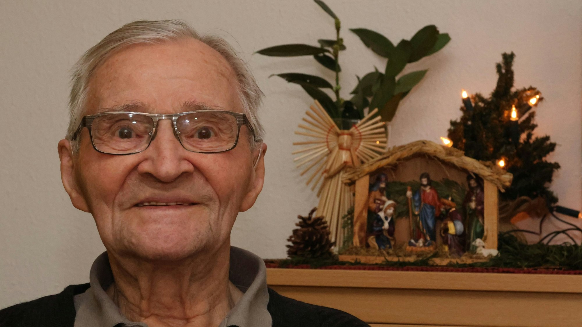 Ein alter Mann steht neben einer Weihnachtskrippe.