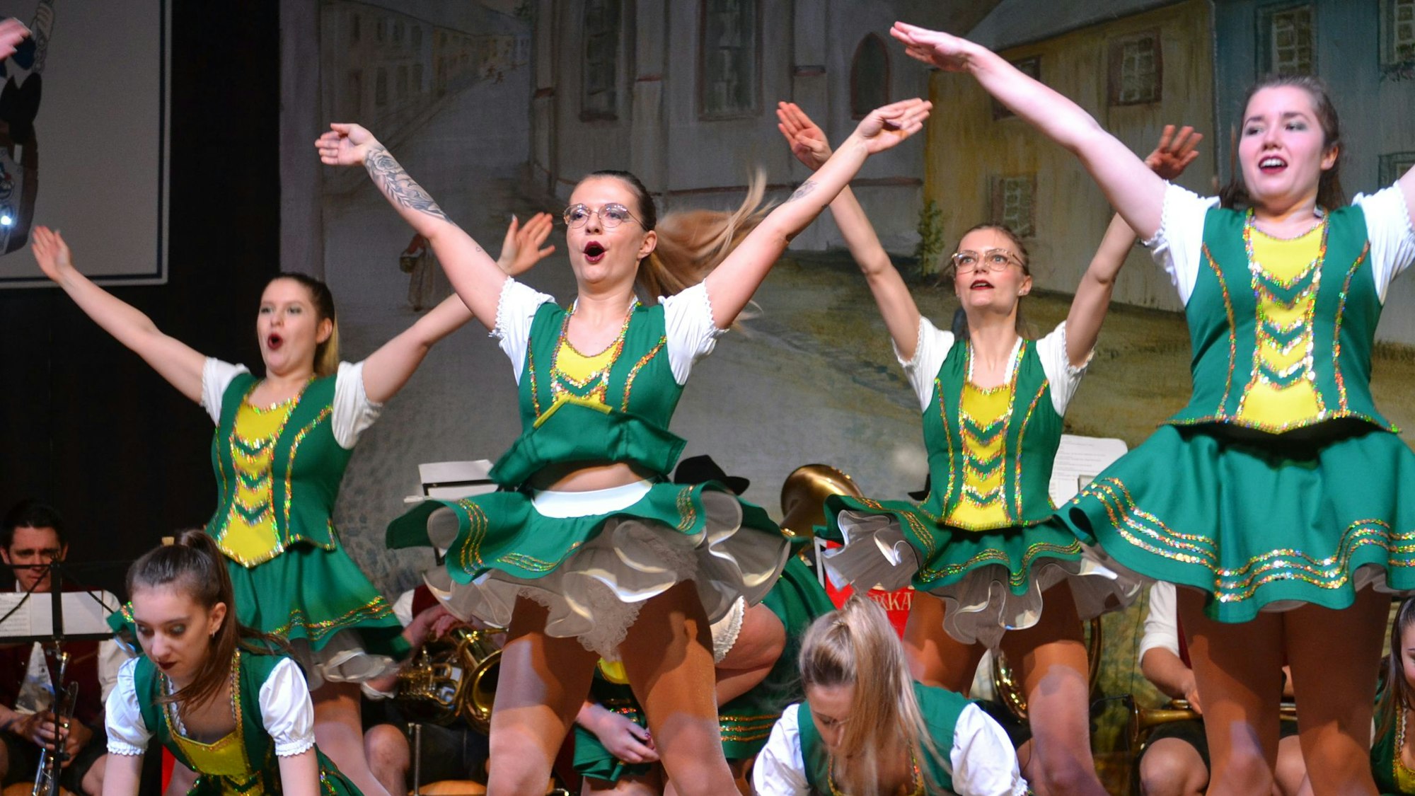 Tänzerinnen der Hovener Jungkarnevalisten zeigen auf der Bühne ihr Programm, die Arme in die Höhe gestreckt. Sie tragen grün-gelbe Kostüme.