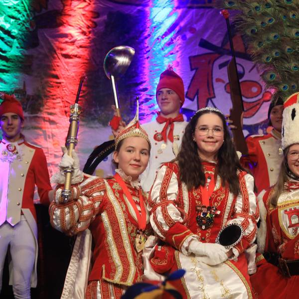 Prinz Ella I., Jungfrau Marie und Bauer Pia (v.l.) stehen in vollem Kinderdreigestirns-Ornat auf der Bühne.