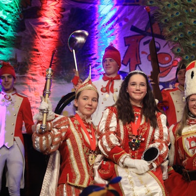 Prinz Ella I., Jungfrau Marie und Bauer Pia (v.l.) stehen in vollem Kinderdreigestirns-Ornat auf der Bühne.