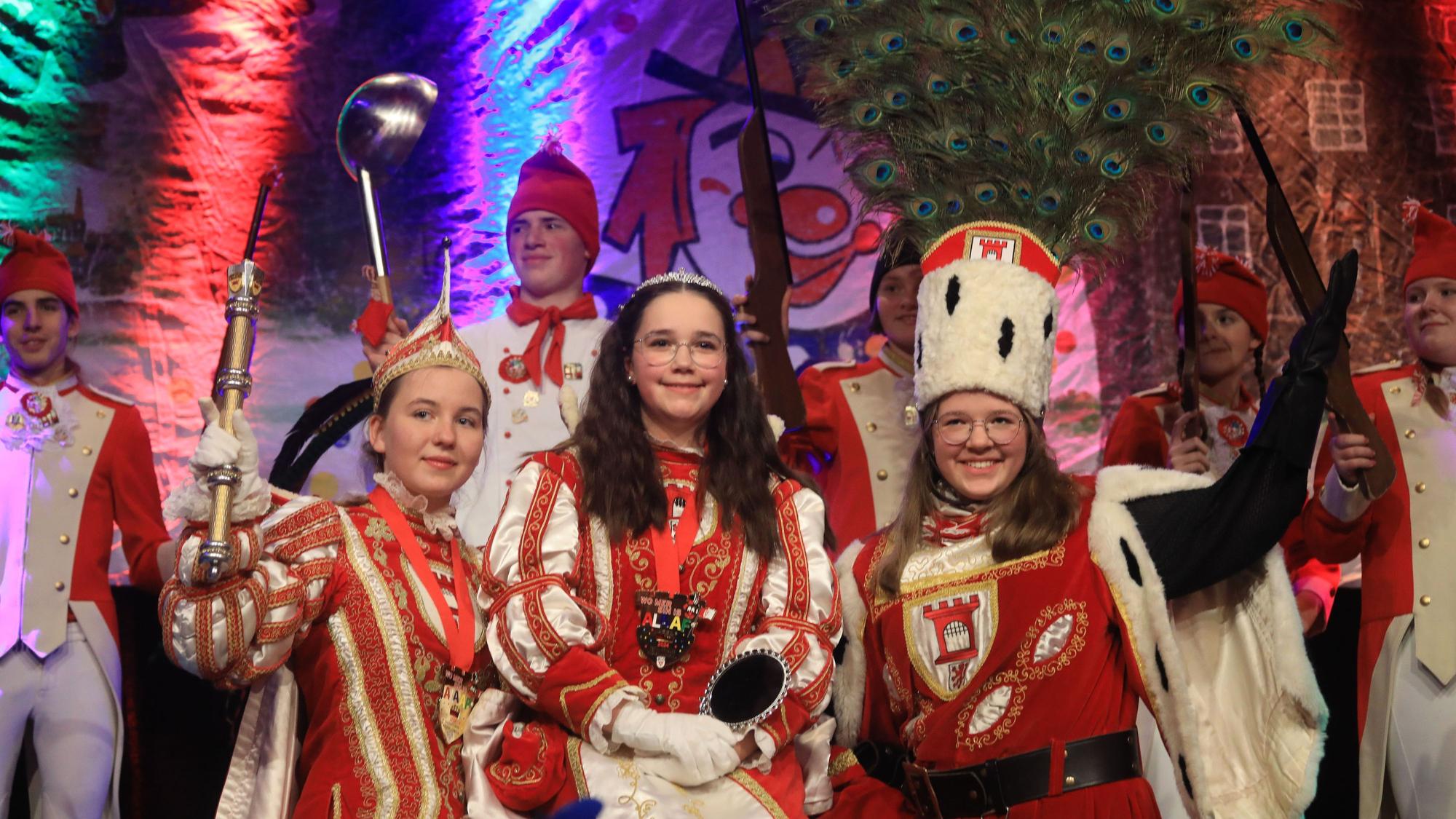 Prinz Ella I., Jungfrau Marie und Bauer Pia (v.l.) stehen in vollem Kinderdreigestirns-Ornat auf der Bühne.