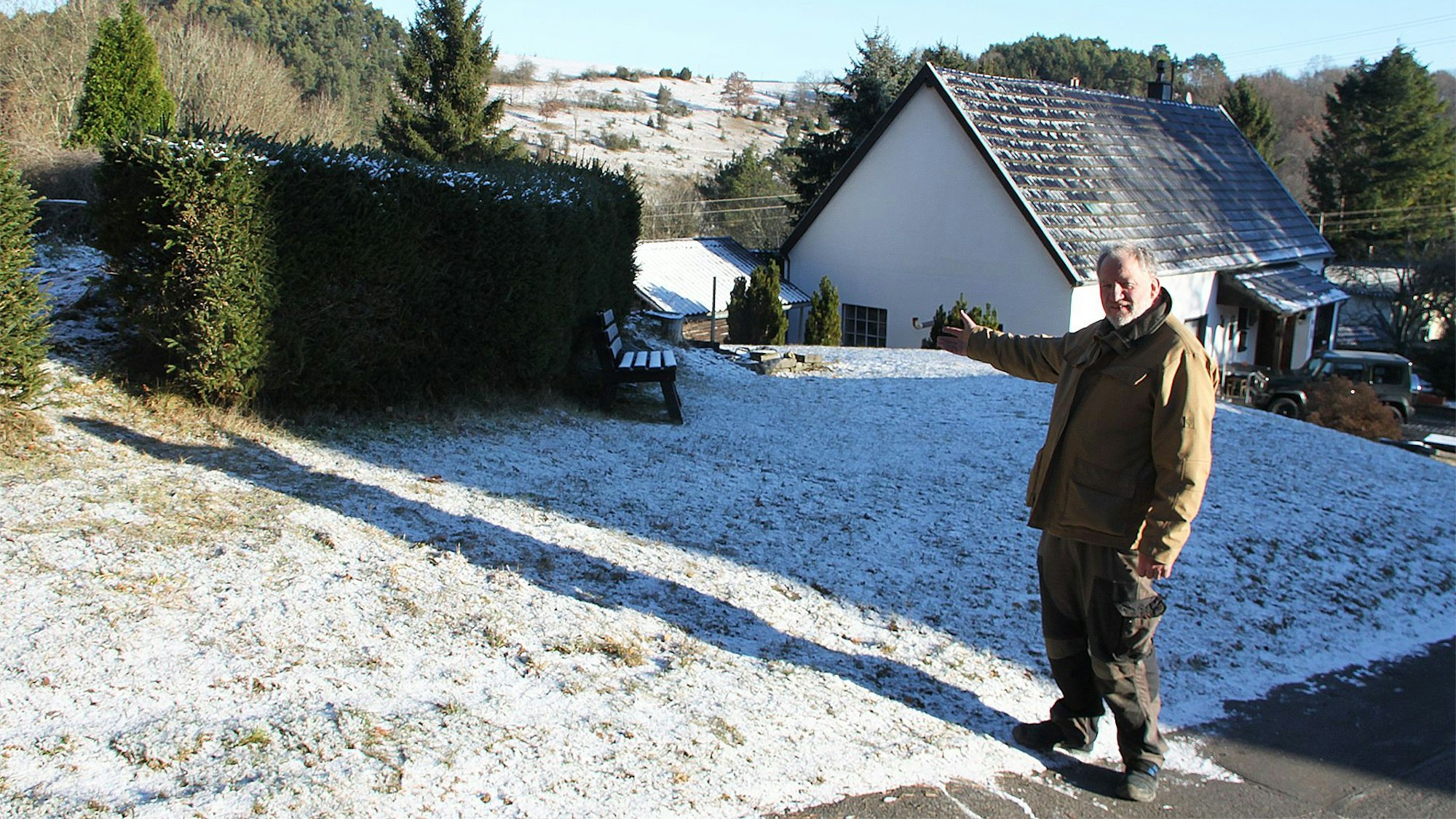Ein Mann zeigt auf eine mit Schnee bedeckte Wiese. Hier wird eine neue Garage für die Feuerwehr in Ahrhütte gebaut.