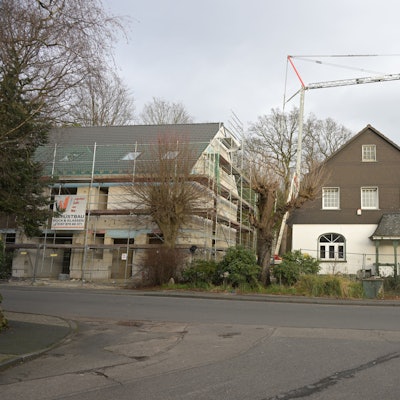 Rechts steht der Altbau, links daneben der Rohbau mit für ein Doppelhaus mit Gerüst.