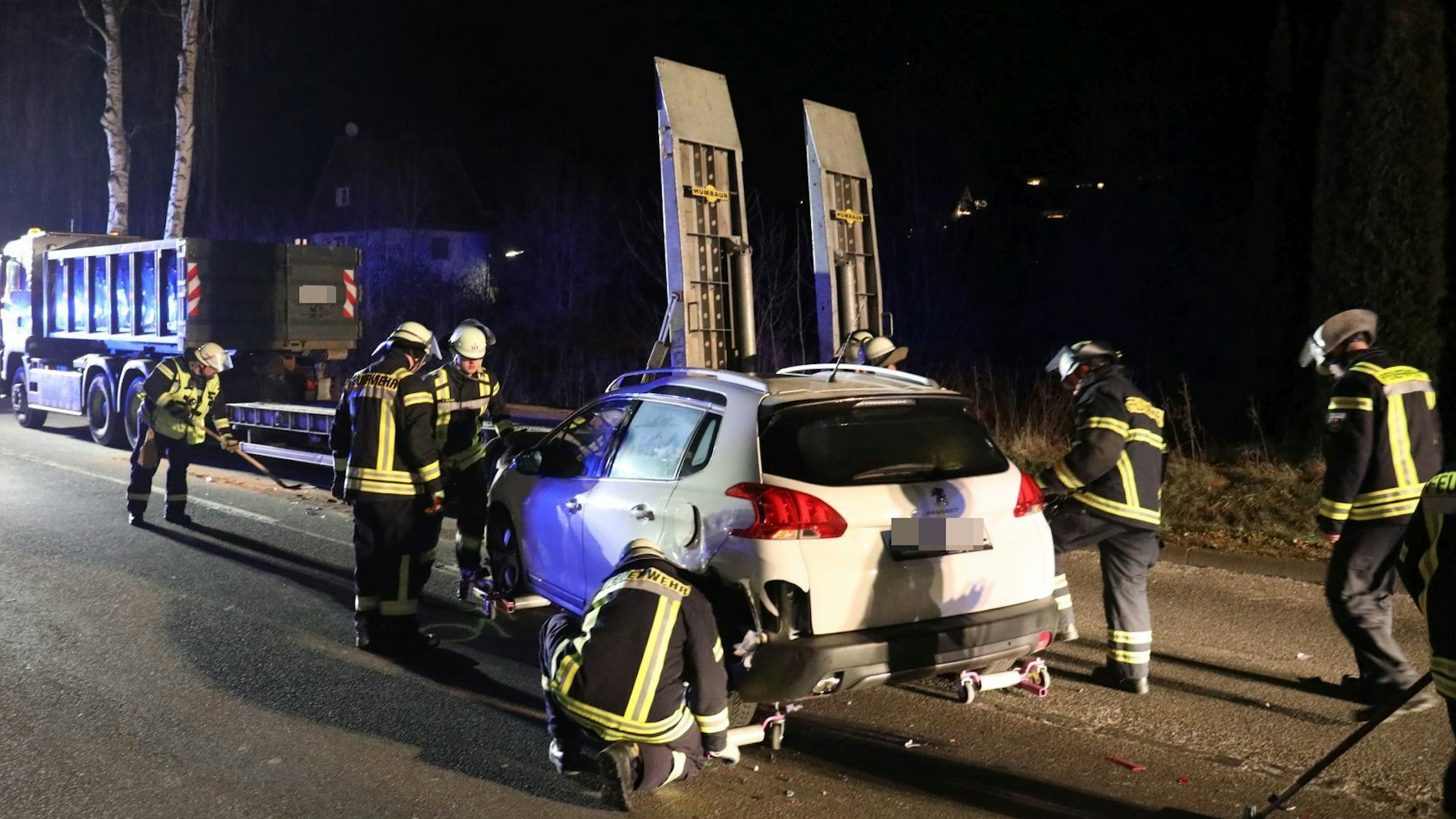 Feuerwehrleute sichern einen weißen Pkw, im Hintergrund steht ein Lastwagen mit Tieflader.