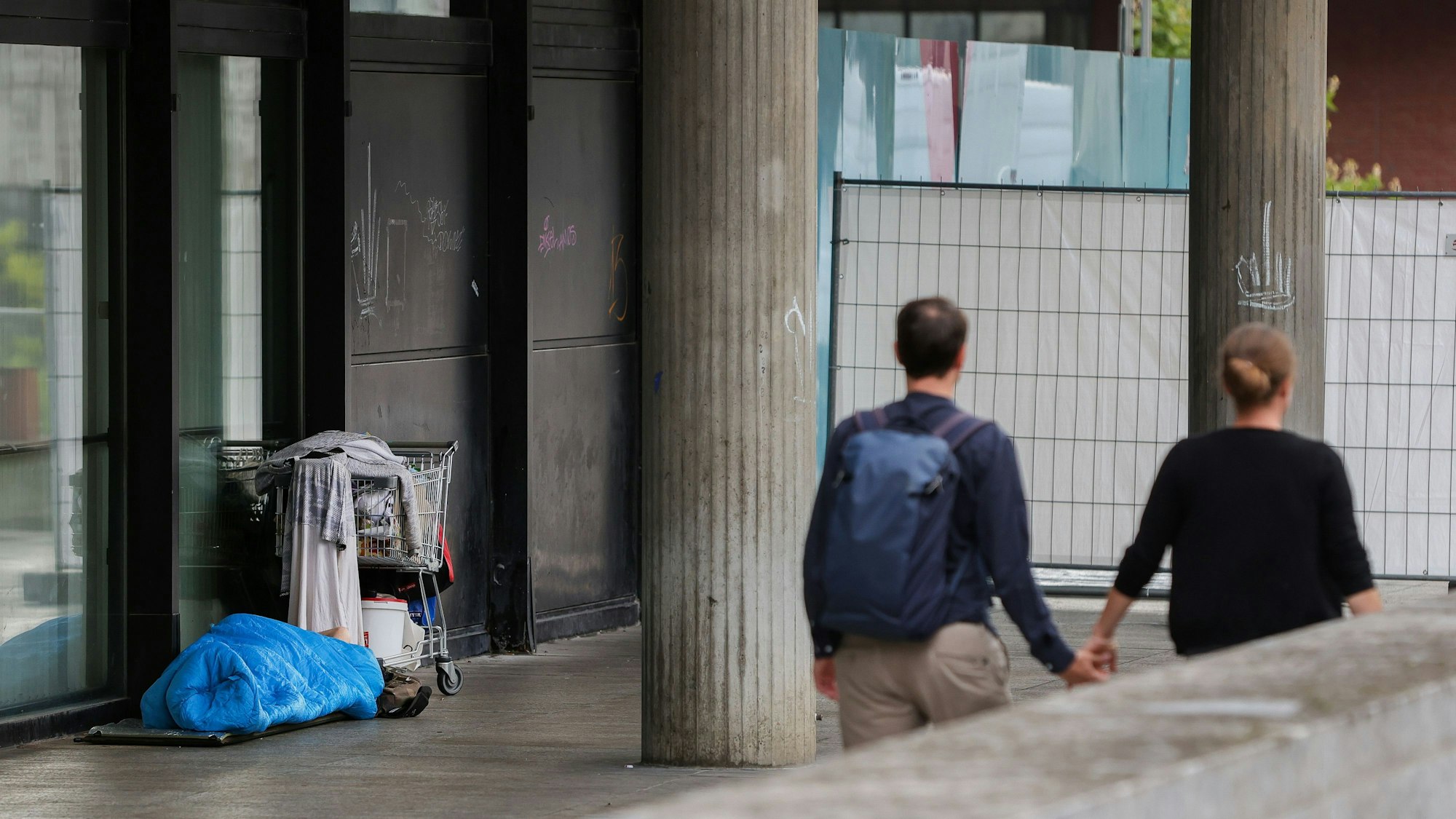 Eine Person schläft vor dem Römisch-Germanischen Museum in einem Schlafsack neben einem Einkaufswagen.