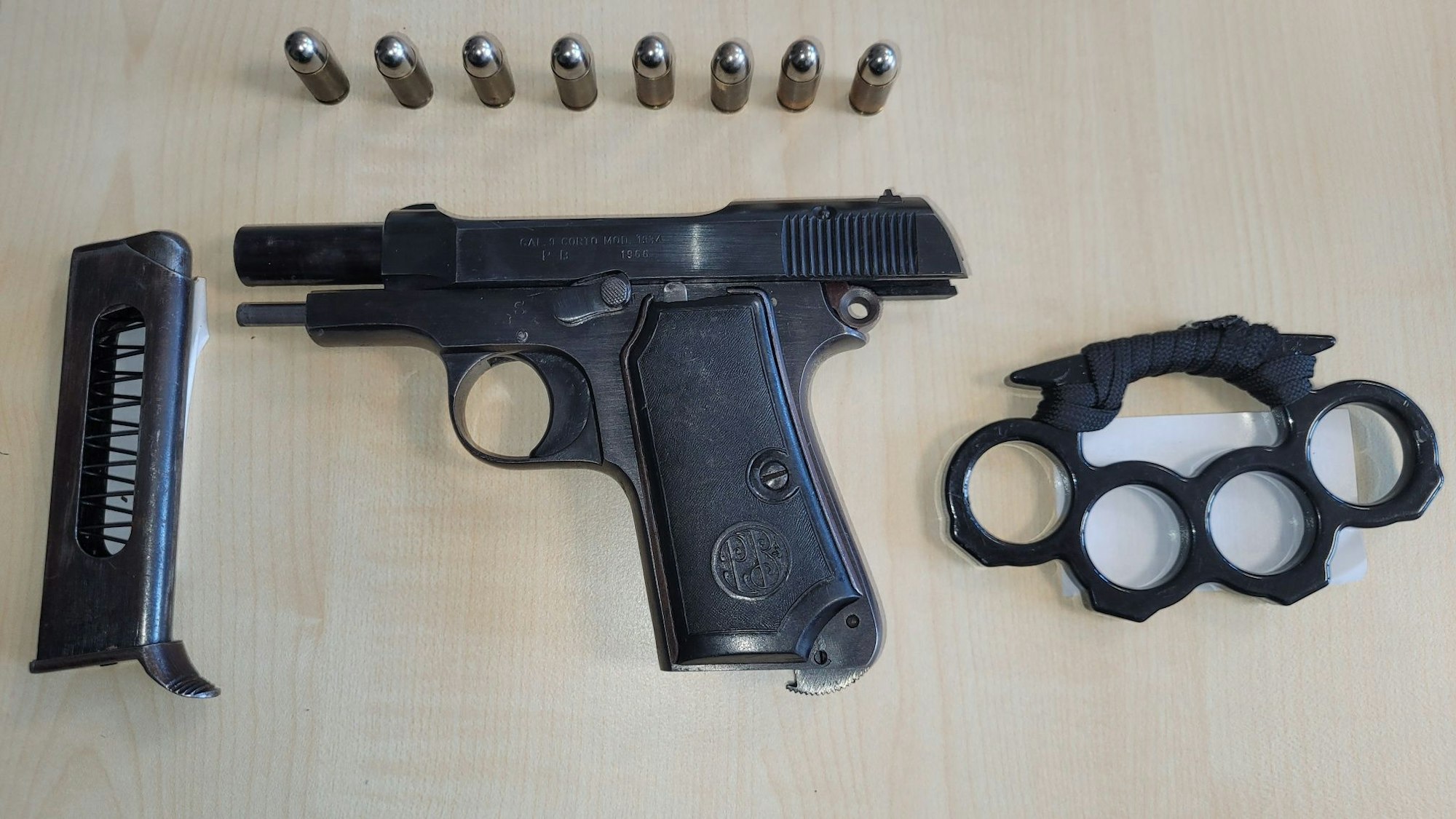 Eine Schusswaffe, ein passendes Magazin und acht Patronen liegen neben einem Schlagring auf einem Tisch.