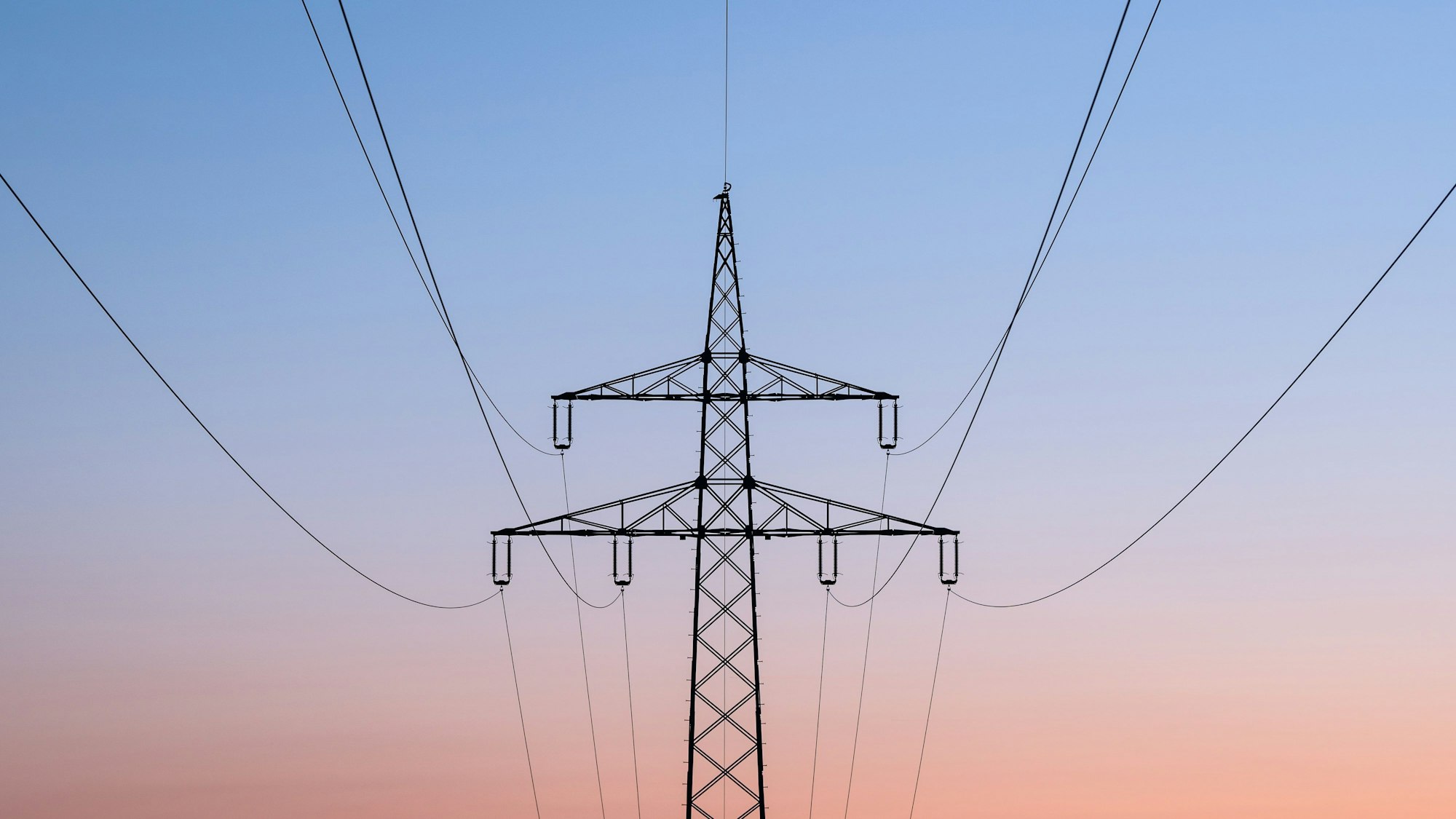 Ein Strommast ist bei Sonnenaufgang als Silhouette zu sehen.