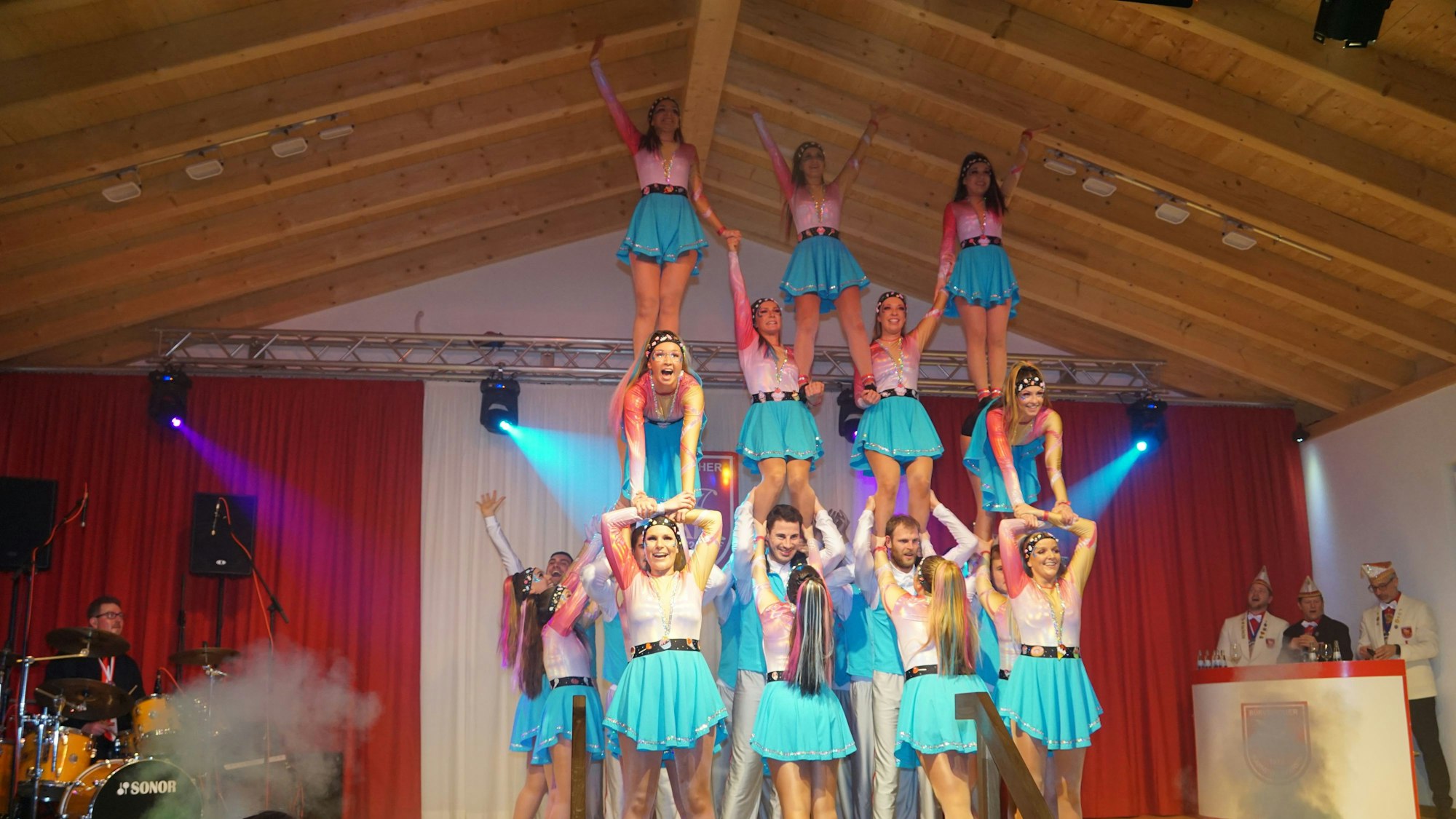 Die Tänzerinnen und Tänzer der Gruppe Bürvenicher Danzspektakel bilden auf der Bühne eine dreistöckige Menschenpyramide. Sie tragen blau-weiße Kostüme.