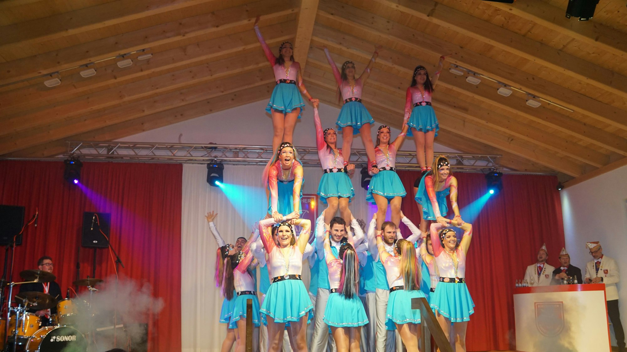 Die Tänzerinnen und Tänzer der Gruppe Bürvenicher Danzspektakel bilden auf der Bühne eine dreistöckige Menschenpyramide. Sie tragen blau-weiße Kostüme.