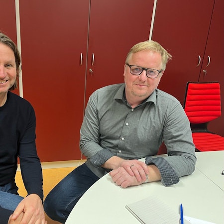 Zwei Lehrer sitzen im Sekretariat einer Schule.