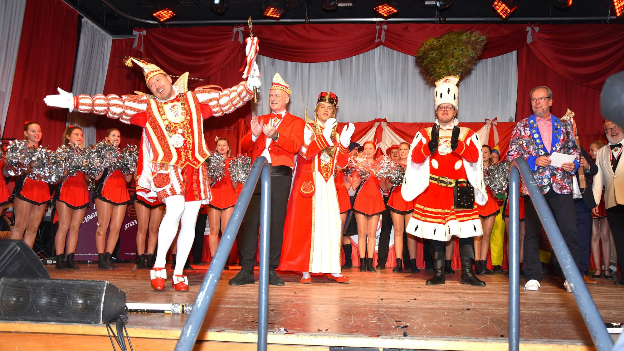 Ein Dreigestirn und eine Tanzgruppe stehen auf einer Bühne.