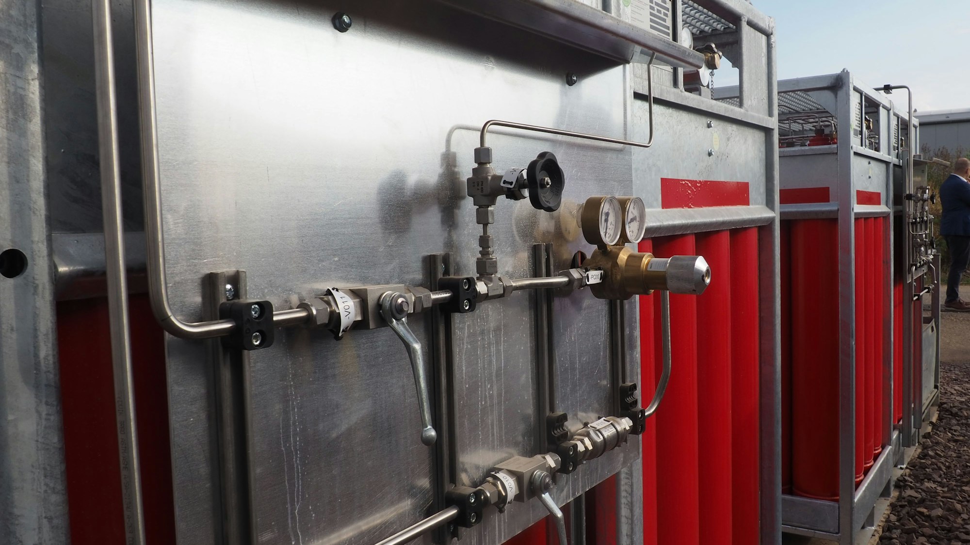 Das Bild zeigt eine Anlage mit Leitungen und Ventilen, im Hintergrund die Flaschen mit Wasserstoff.