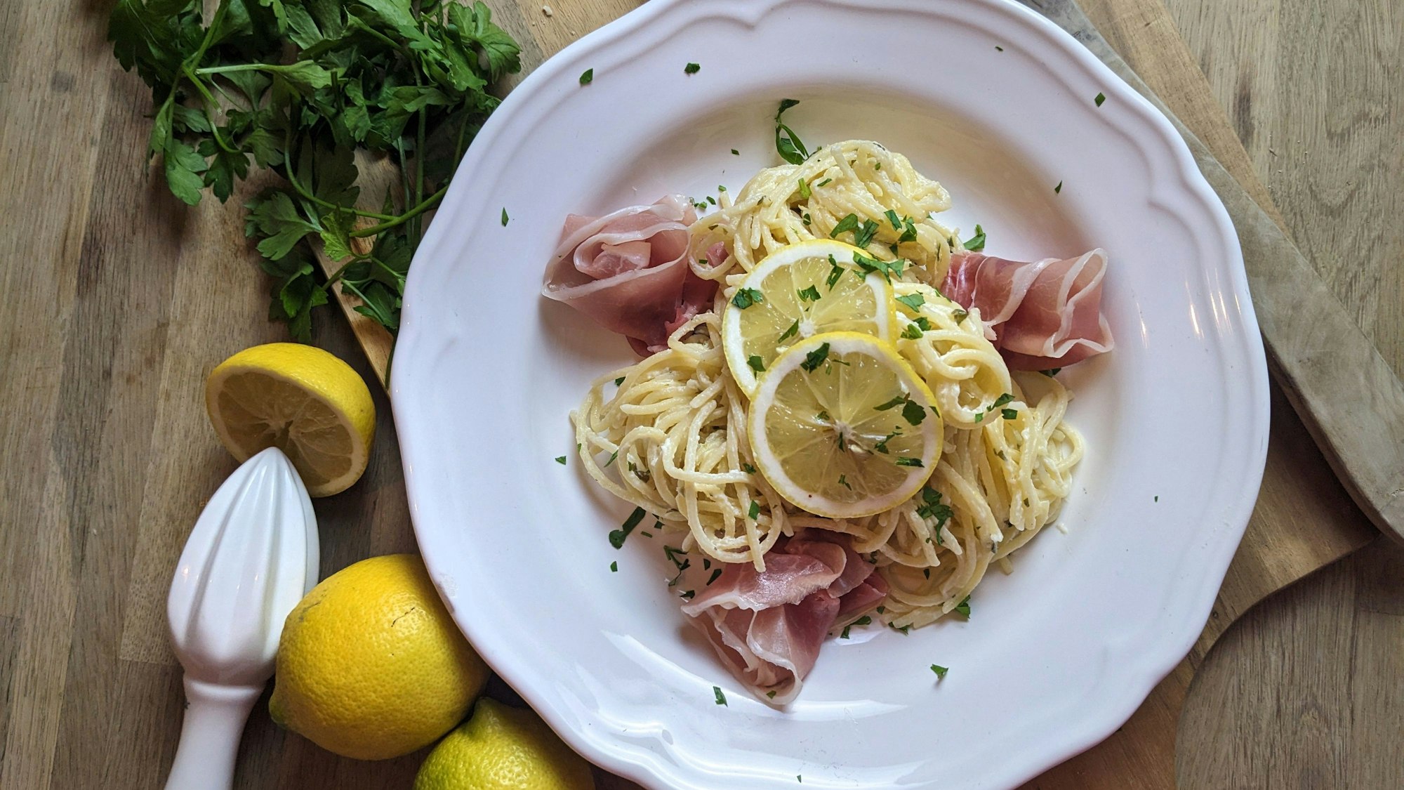 Spaghetti liegen auf einem Teller, mit Zitronenscheiben und Parmaschinken.