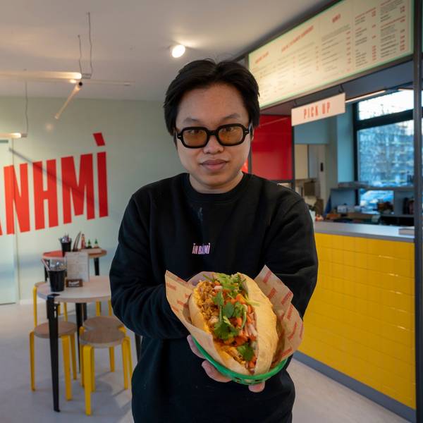 Ein Mann steht in einem Restaurant und hält ein Sandwich in die Kamera.