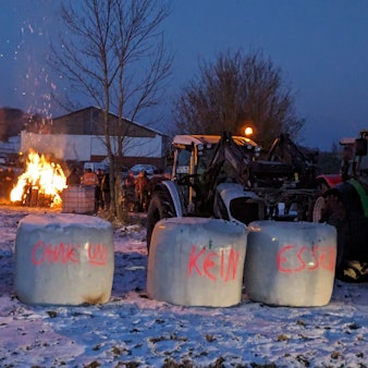 Ein Traktor und Strohballen mit Protest-Aufschriften stehen vor einem Feuer.