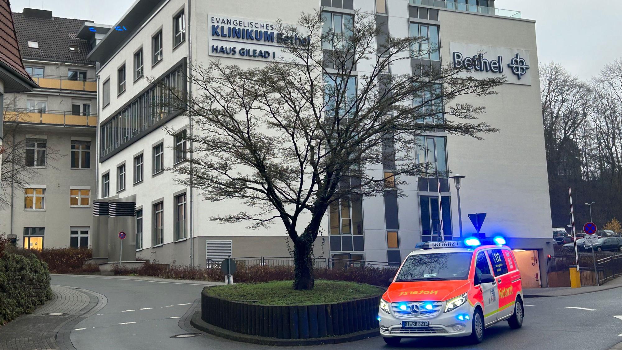 Blick auf das Gebäude des Klinikums Bethel in Bielefeld. Ein Rettungswagen mit Blaulicht fährt vorbei.